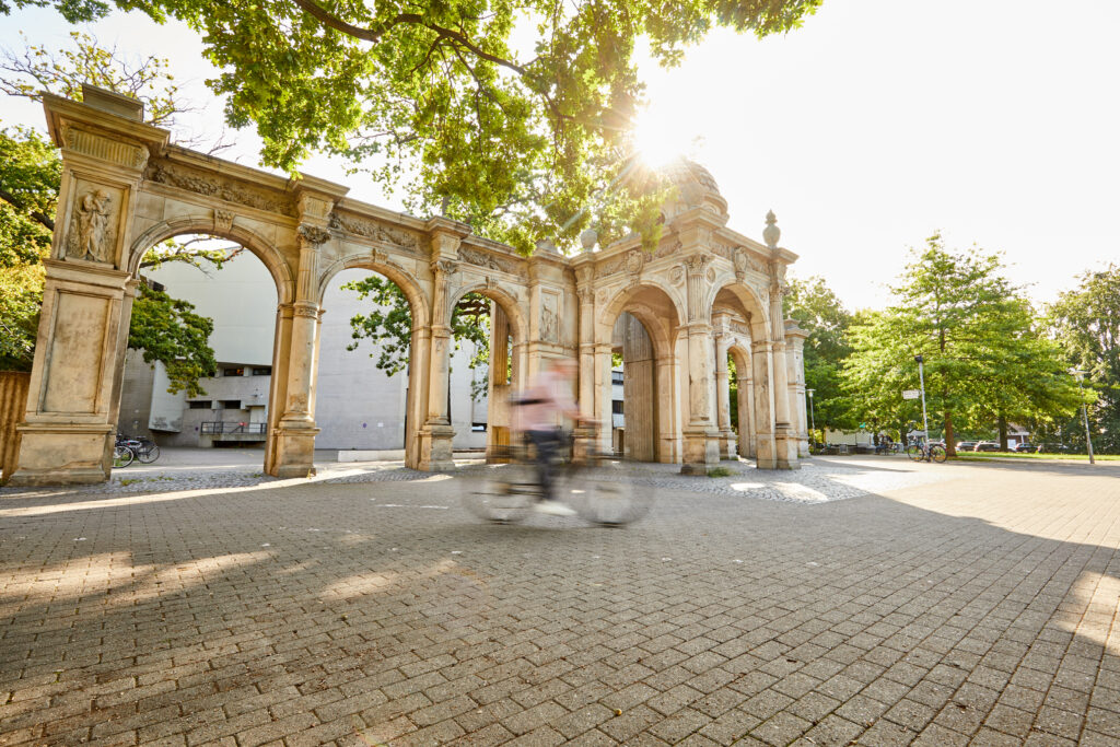 Ein*e Radfahrer*in fährt durch die Geschwindigkeit "verwischt" vor dem "Neuen Haus" am Emmichplatz in Hannover