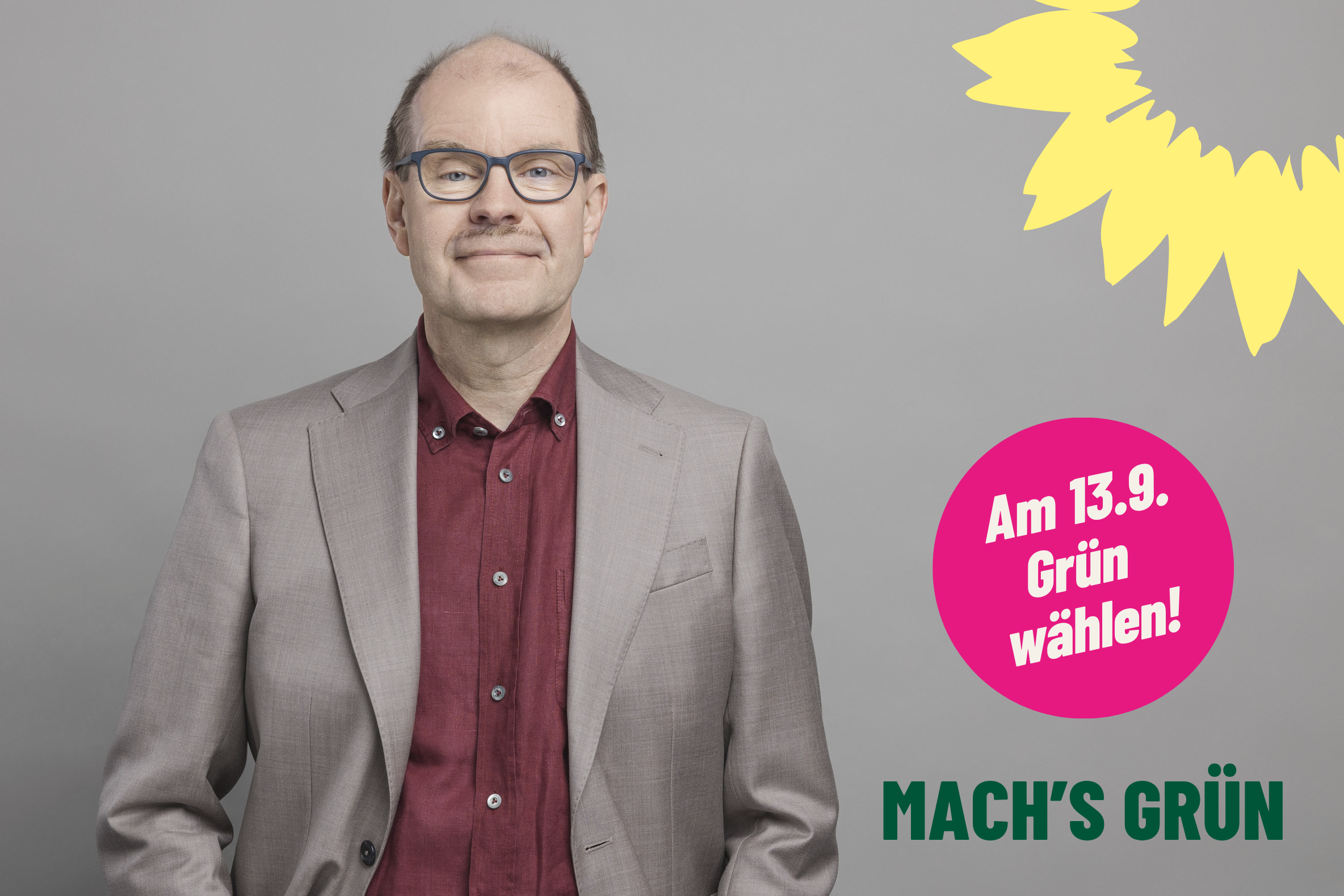 Portrait von mir vor neutralem Hintergrund. Ich trage ein dunkerrotes Hemd und ein helles Sakko. auf der rechten Seite befindet sich das angeschnittene Sonneblumenlogo der Grünen, ein pinker Kreis mit dem Text "Am 13.9. Grün wählen" und der Claim "MACH'S GRÜN"
